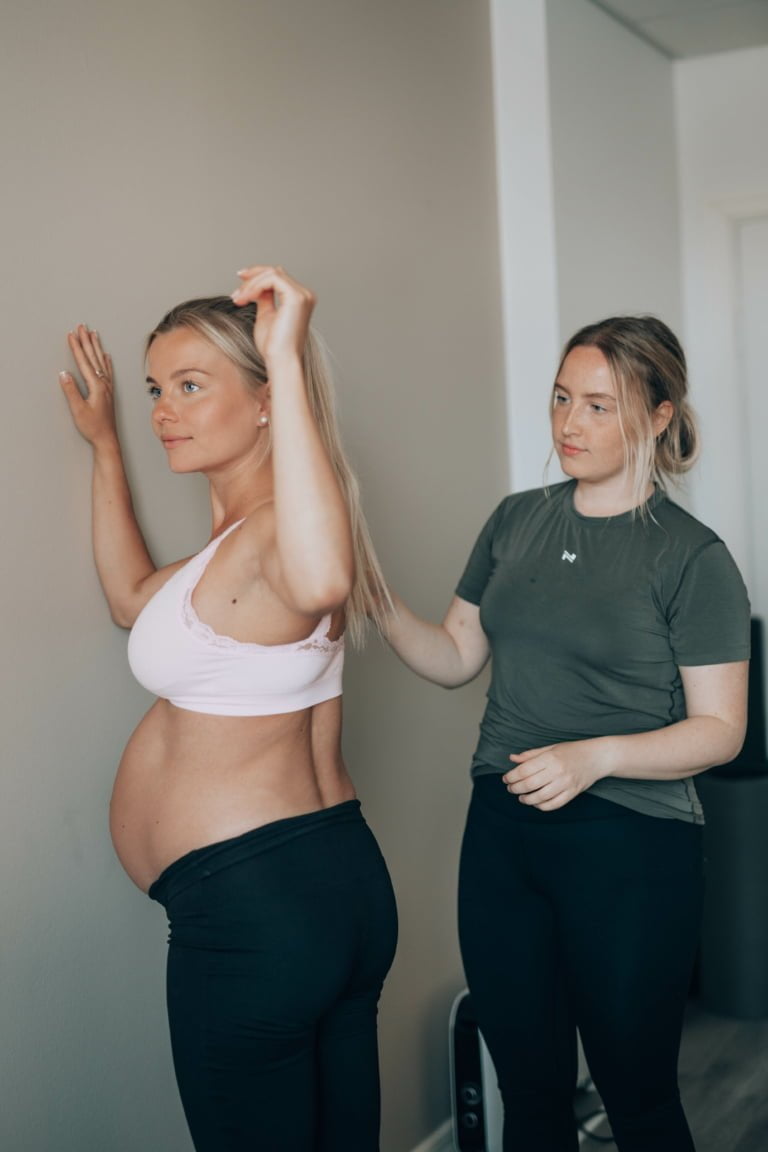 Fysioterapia raskausaikana, odottava aiti ja fysioterapeutti tekevat liiketta.